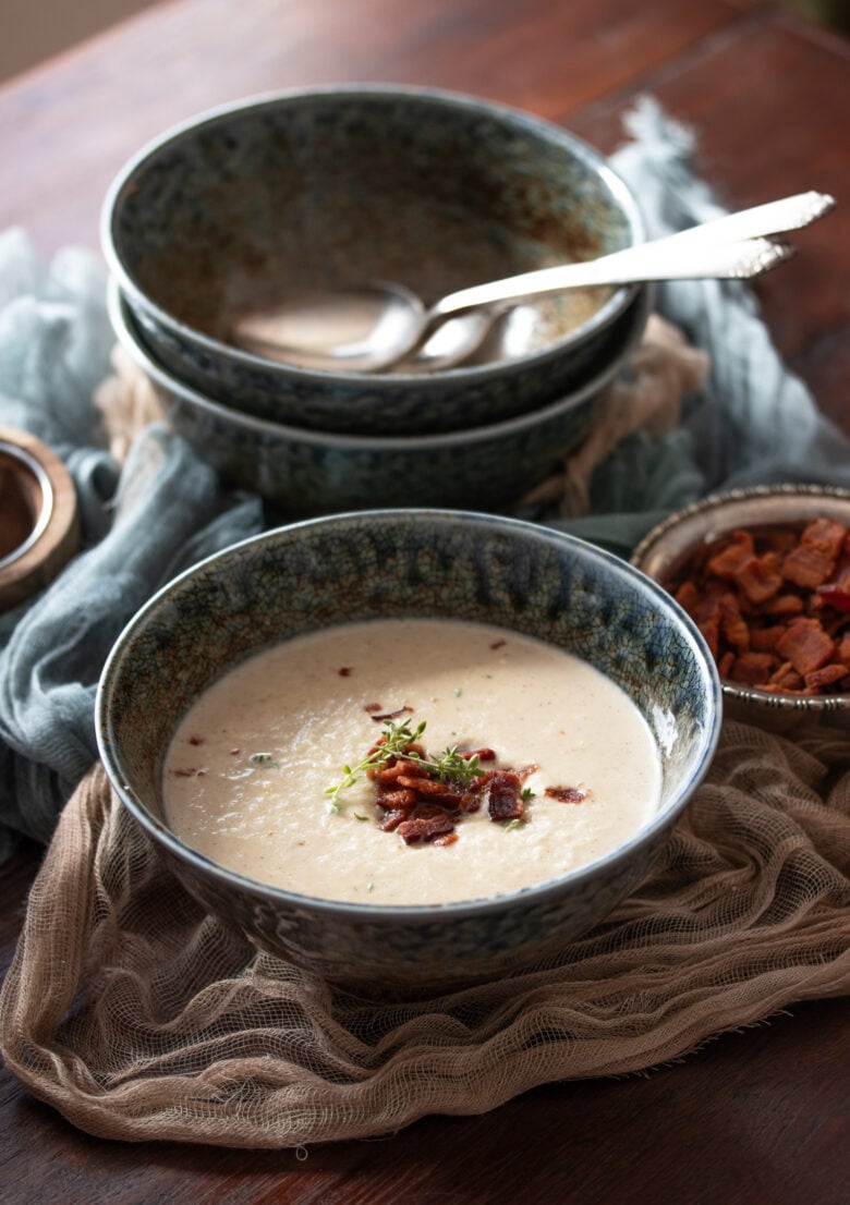 Roasted Cauliflower Soup in a blue bowl with bacon bits next to it